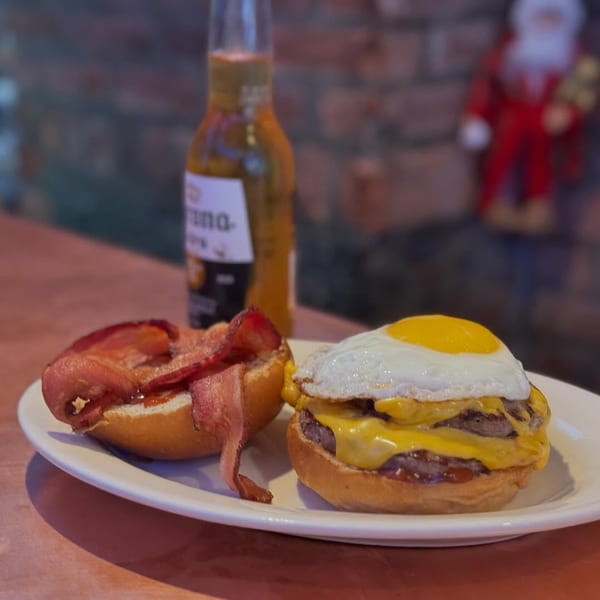 A double cheeseburger with a fried egg and bacon on a bun, next to a beer bottle.