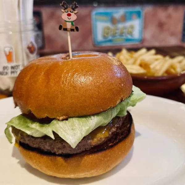 A beef burger with cheese and lettuce, topped with a reindeer pick, served with fries.