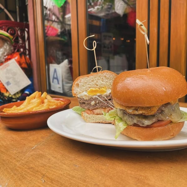 Two gourmet burgers, one cut in half revealing a fried egg, with a side of fries.