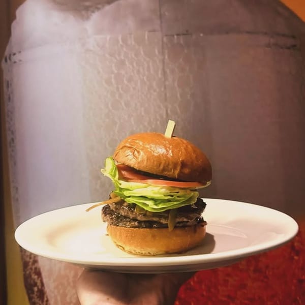 A double patty burger with lettuce, tomato, and caramelized onions on a white plate.