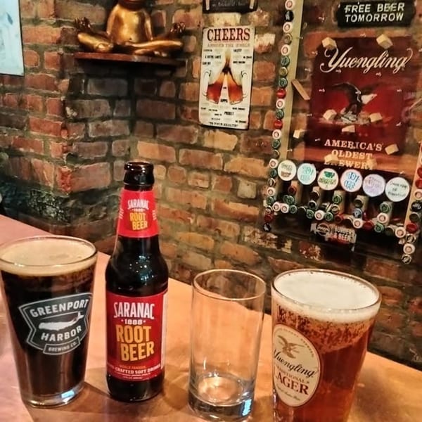 Two beers, a root beer bottle, and an empty glass on a bar with a brick wall background.