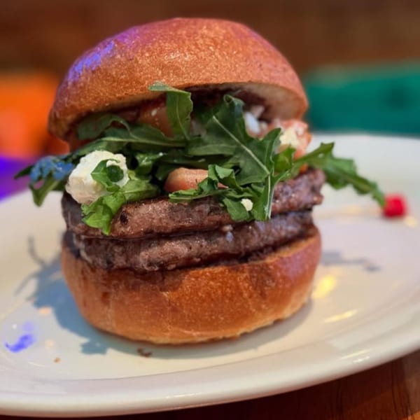 Double patty burger with arugula, tomatoes, and feta cheese on a white plate.