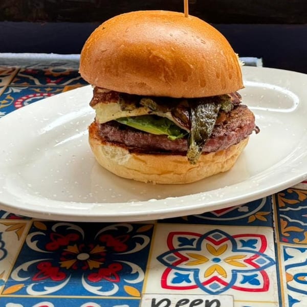 A Burgers and Beer burger with a thick patty, cheese, avocado, and green chiles on a white plate.