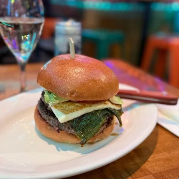 A Burgers and Beer burger with cheese, avocado, and green chiles on a white plate.