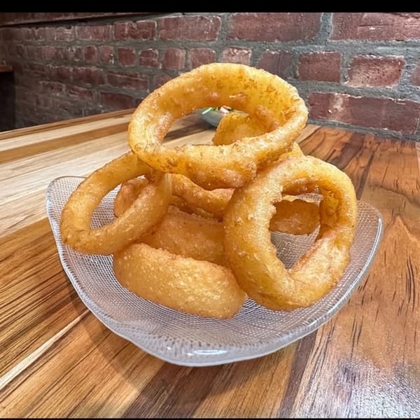 A clear glass dish filled with golden-brown, crispy onion rings on a wooden table.